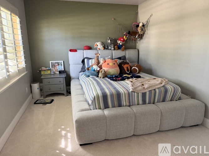 A bedroom with a bed, striped comforter, and a shelf with stuffed animals.
