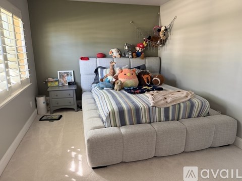A bedroom with a bed, striped comforter, and a shelf with stuffed animals.