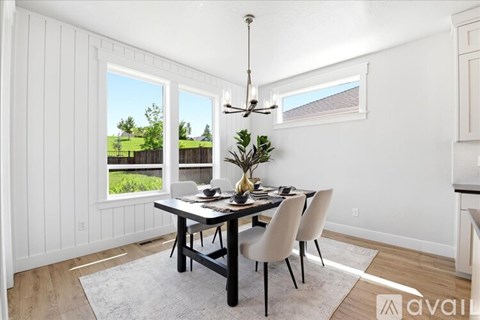 A dining room with a table set for two and a view of a green lawn and a house.