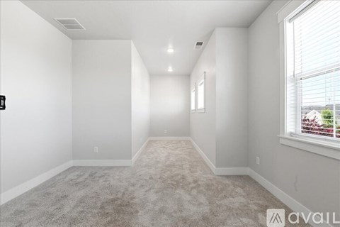 A spacious, empty room with carpeted floor and a window with blinds.