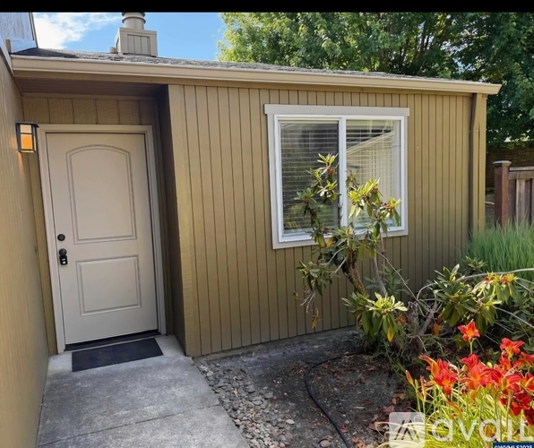 A small house with a white door and a window with a plant in front.
