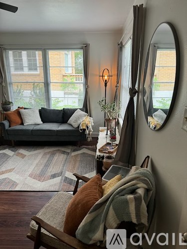 A living room with a grey couch, a wooden chair, a rug, and a mirror on the wall.
