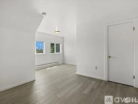 A room with white walls and wooden flooring, with a door on the right side.