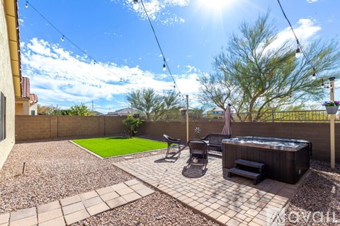 A backyard with a hot tub, patio furniture, and a tree.