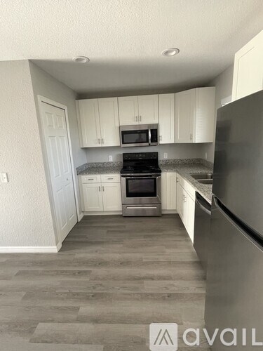 A kitchen with a black fridge, white cabinets and a black stove top.
