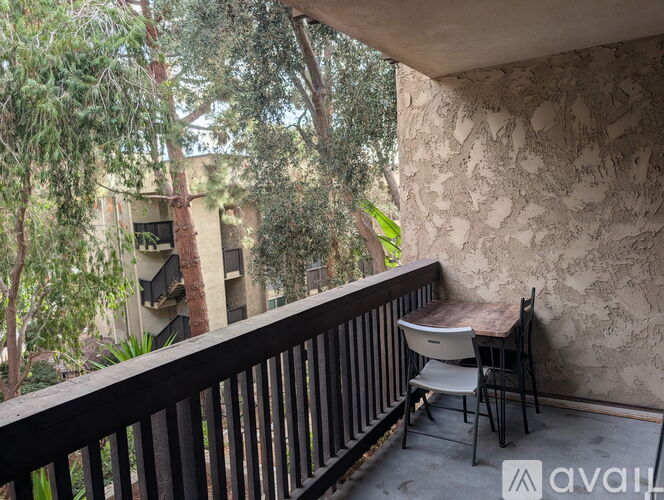 A balcony with a table and chairs overlooks a tree-filled courtyard.