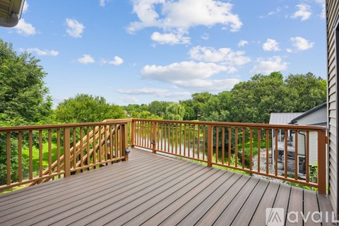 A wooden deck with a railing and a view of trees and sky.
