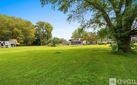 A grassy field with trees and a house in the distance.
