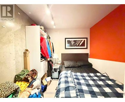 A bedroom with a bed, a dresser, and a closet full of clothes.