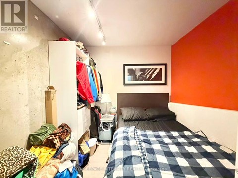 A bedroom with a bed, a dresser, and a closet full of clothes.