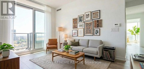A living room with a grey couch, a brown armchair, a coffee table, and a large window with a view of the city.