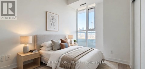 A bedroom with a large bed, a nightstand with a lamp, and a framed picture on the wall.