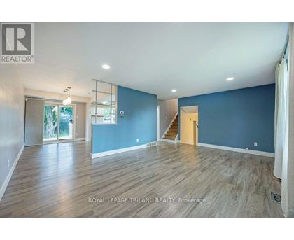 A spacious room with wooden flooring and a staircase leading to another room.