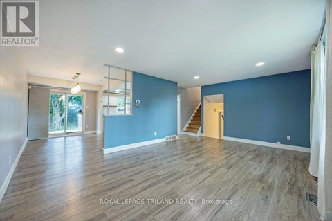 A spacious room with wooden flooring and a staircase leading to another room.