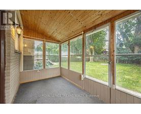 A sunroom with a wooden ceiling and floor, large windows, and a view of a backyard.