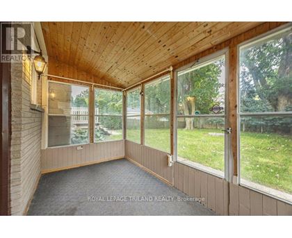 A sunroom with a wooden ceiling and floor, large windows, and a view of a backyard.