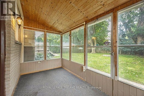A sunroom with a wooden ceiling and floor, large windows, and a view of a backyard.