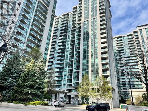 A tall building with many windows is surrounded by trees and has a car parked in front.