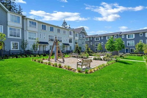 A playground area with a swing set and a wooden bench is located in the front yard of a residential building.