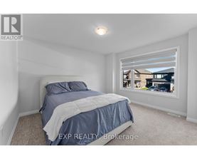 A bedroom with a bed, carpeted floor, and a window showing a view of a house and cars outside.