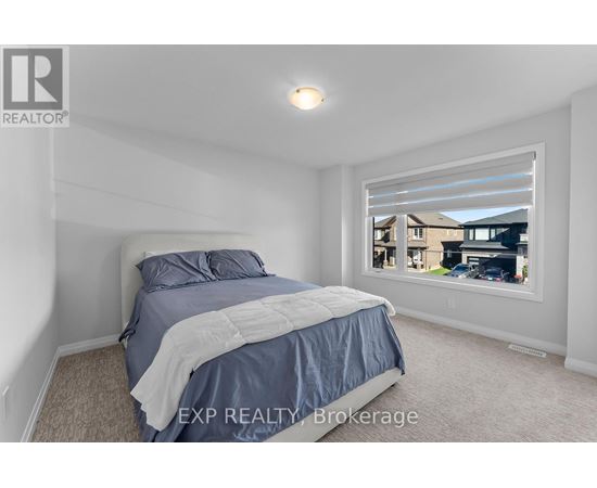 A bedroom with a bed, carpeted floor, and a window showing a view of a house and cars outside.