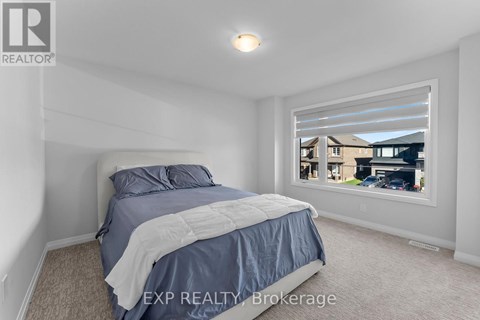 A bedroom with a bed, carpeted floor, and a window showing a view of a house and cars outside.