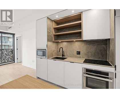 A modern kitchen with white cabinets and a wooden shelf above the sink.