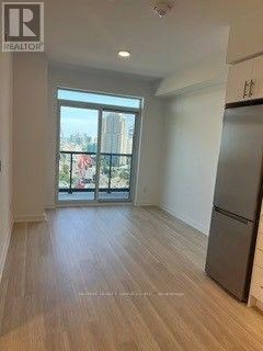 A spacious room with wooden flooring and a large window overlooking a balcony.