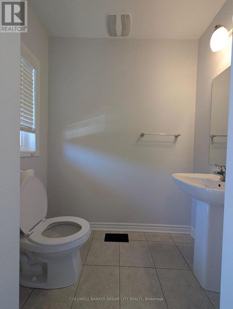 A white toilet sits in a small bathroom with a sink and mirror.