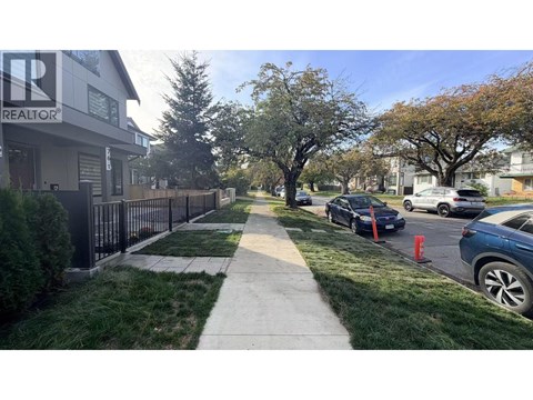 A residential street with cars parked on the side and a realtor's office in the background.