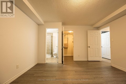 A realtor photo of a white bedroom with wood floors and a doorway leading to a bathroom.