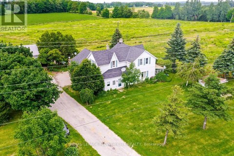 A white house with a grey roof is surrounded by green trees.