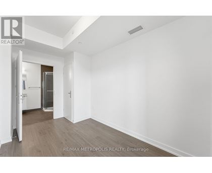 A spacious room with wooden flooring and white walls, with a doorway leading to another room.