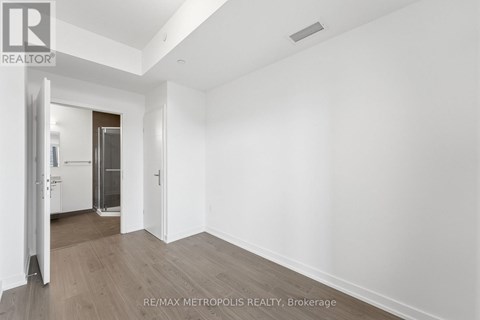 A spacious room with wooden flooring and white walls, with a doorway leading to another room.