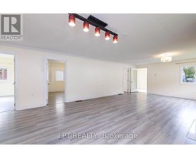 A spacious room with wooden flooring and white walls, with a ceiling light and a painting on the wall.