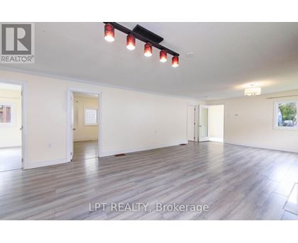 A spacious room with wooden flooring and white walls, with a ceiling light and a painting on the wall.