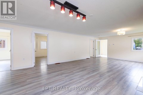 A spacious room with wooden flooring and white walls, with a ceiling light and a painting on the wall.