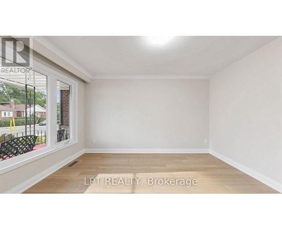 A room with a window and a view of a street and houses.