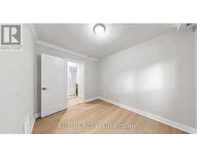 A spacious room with white walls and wooden flooring, featuring a doorway leading to another room.