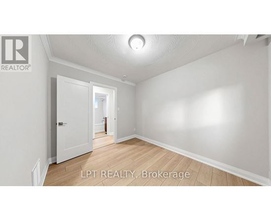A spacious room with white walls and wooden flooring, featuring a doorway leading to another room.