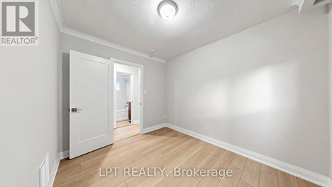A spacious room with white walls and wooden flooring, featuring a doorway leading to another room.