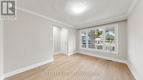 A room with a window showing a view of a street with houses and trees.