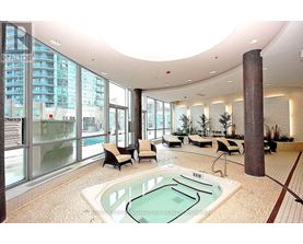 A large indoor swimming pool with a hot tub in the middle of a spacious room with a curved ceiling and a view of a building outside the windows.