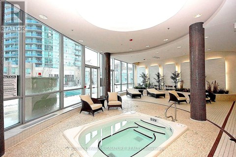 A large indoor swimming pool with a hot tub in the middle of a spacious room with a curved ceiling and a view of a building outside the windows.