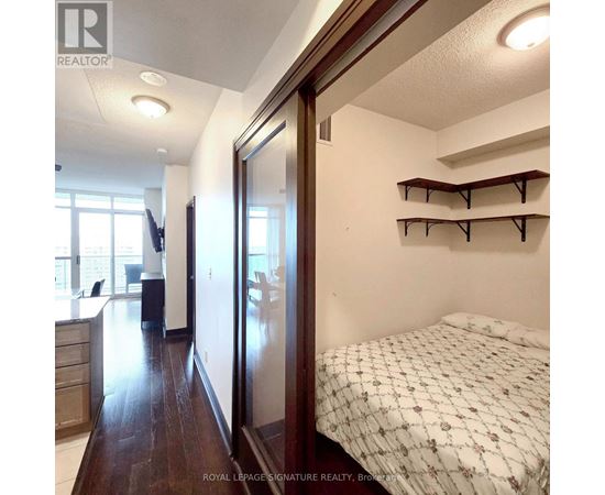 A bedroom with a bed, a desk, and a kitchen area.
