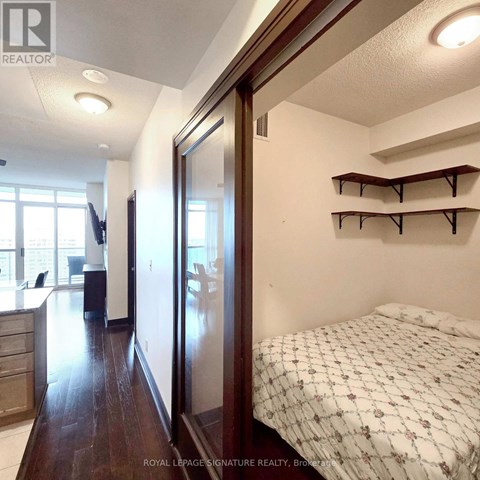 A bedroom with a bed, a desk, and a kitchen area.