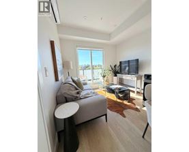A living room with a grey couch, a white chair, and a flat screen TV mounted on the wall.
