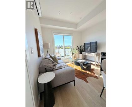 A living room with a grey couch, a white chair, and a flat screen TV mounted on the wall.