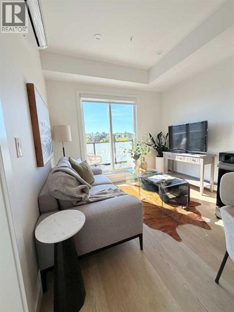 A living room with a grey couch, a white chair, and a flat screen TV mounted on the wall.