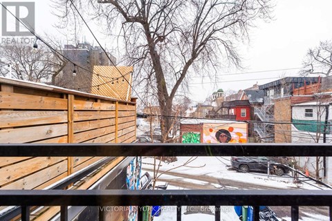 A view from a balcony overlooking a snowy street with buildings and a car.
